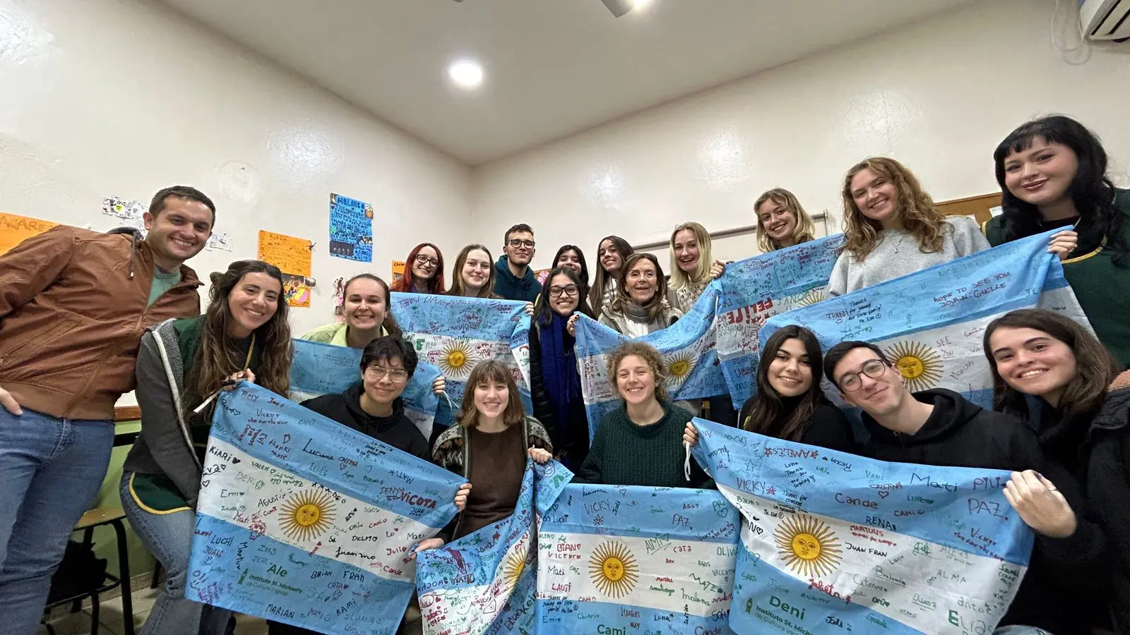 Despedida de voluntarias internacionales junto a estudiantes en escuela argentina con banderas firmadas, en el marco de un programa de intercambio cultural de Consultora Puentes.